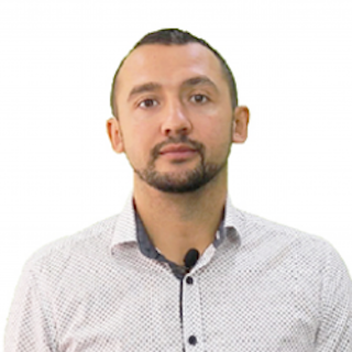 Man with short hair and beard, wearing a patterned shirt, standing against a white background.