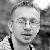 Black and white portrait of a smiling man with glasses, short hair, blurred background.